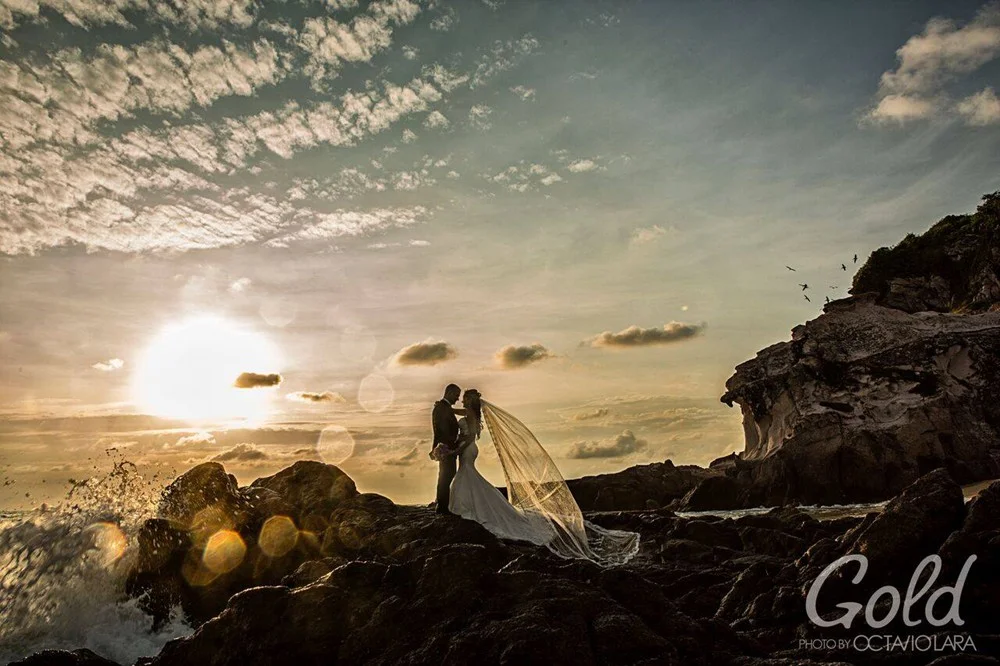 Novios sobre una costa rocosa bajo un cielo al atardecer