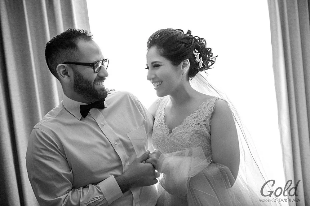 Novios sonriendo frente a una ventana, en blanco y negro