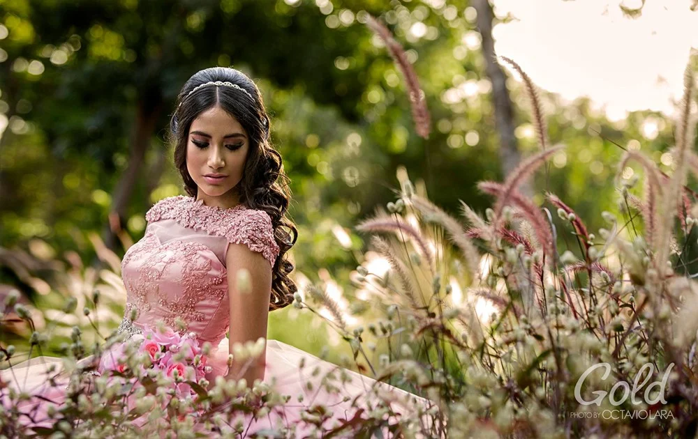 Quinceañera con vestido rosa entre flores de un jardín