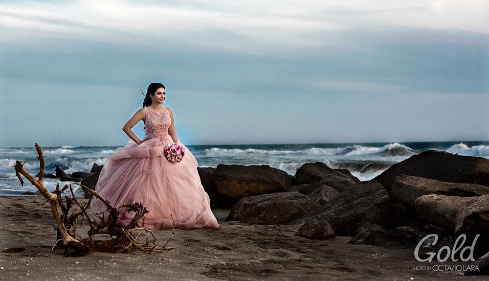 Quinceañera con vestido rosa frente a la costa